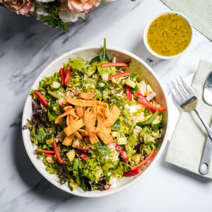 Salad with crispy toppings on a marble surface with flowers and cutlery.