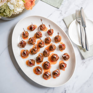 Platter of appetizers on a marble surface with flowers and cutlery in the background