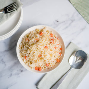 Bowl of rice with carrots on a marble surface with a fork, spoon, and floral decorations.