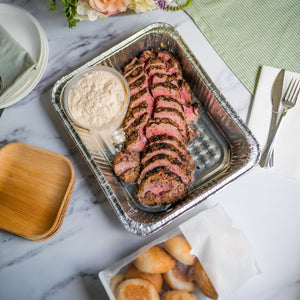 Open image in slideshow, Plated dish of sliced meat with sides on a marble table with flowers and cutlery.
