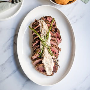 Plated dish of sliced beef with a side of bread on a marble table.