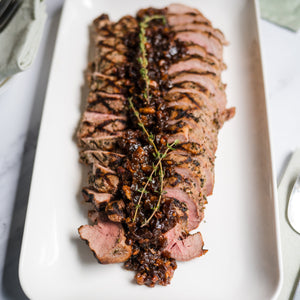 Sliced beef tenderloin on a white plate with a marble background
