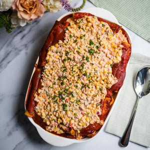 Baked enchilada casserole dish with a crumbly topping on a marble surface with flowers and cutlery.