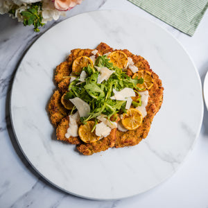 Plated chicken milanese dish with salad on top on a marble surface with flowers in the background