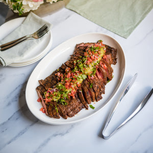 Sliced flank steak with a garnish on a white plate on a marble table.