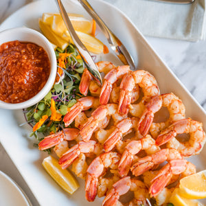 Platter of shrimp with lemon wedges and a side of sauce on a marble surface.
