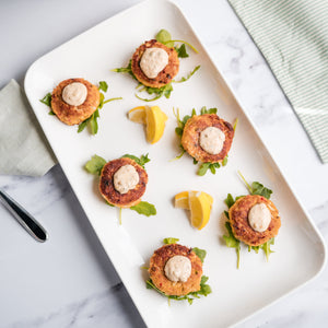 Platter of crab cakes with lemon wedges on a marble surface