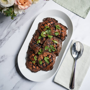 Grilled portobellos with herbs on a white plate with flowers and a spoon in the background.