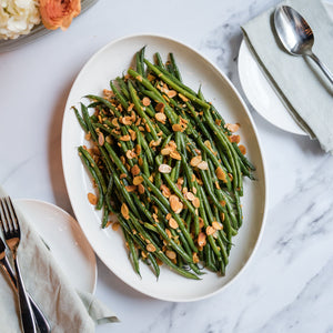 Plated green beans with garnishes on a marble table with flowers and cutlery.