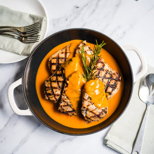 Dish of grilled chicken with a creamy bbq sauce in a black skillet on a marble surface.