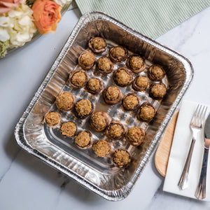Aluminum tray with Italian Sausage Stuffed Mushrooms on a marble surface with flowers and cutlery in the background