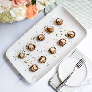 Plated dish of Italian Sausage Stuffed Mushrooms with a floral arrangement on a marble surface