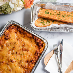 Two pans of food on a table with flowers and cutlery.