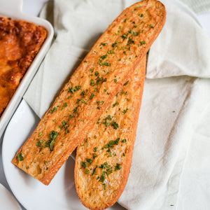 Two pieces of garlic bread with herbs on a white plate with a marble background