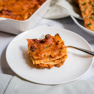 Slice of lasagna on a white plate with a fork, blurred background
