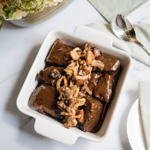 Dish of Madeira Braised Beef Short Ribs with a floral arrangement on a table
