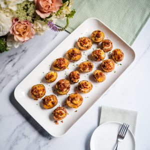 Platter of small round mini twice baked potatoes with a fork and napkin on a marble surface with flowers in the background