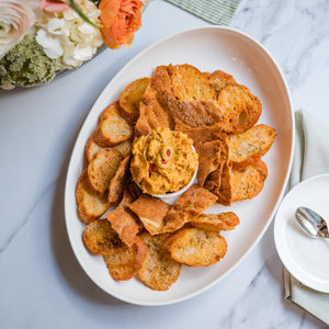 Platter of pimento cheese and chips on a marble surface with flowers and cutlery.