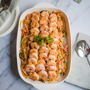 Shrimp dish in a white oval baking dish on a marble surface with a green napkin and silverware.