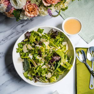 Salad bowl with a side of dressing, flowers, and cutlery on a marble surface