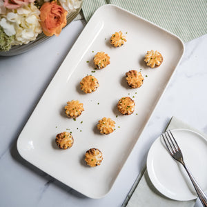 Platter of small round appetizers on a marble surface with flowers and cutlery.